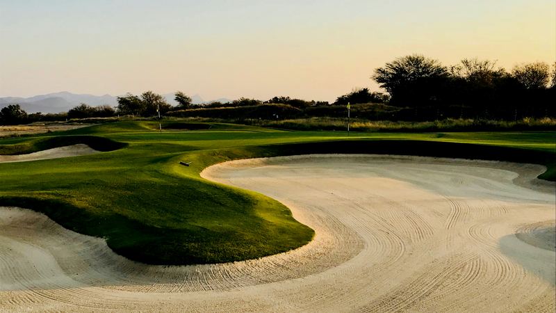 A green ringed by deep raked bunkers, late light across the fairway.
