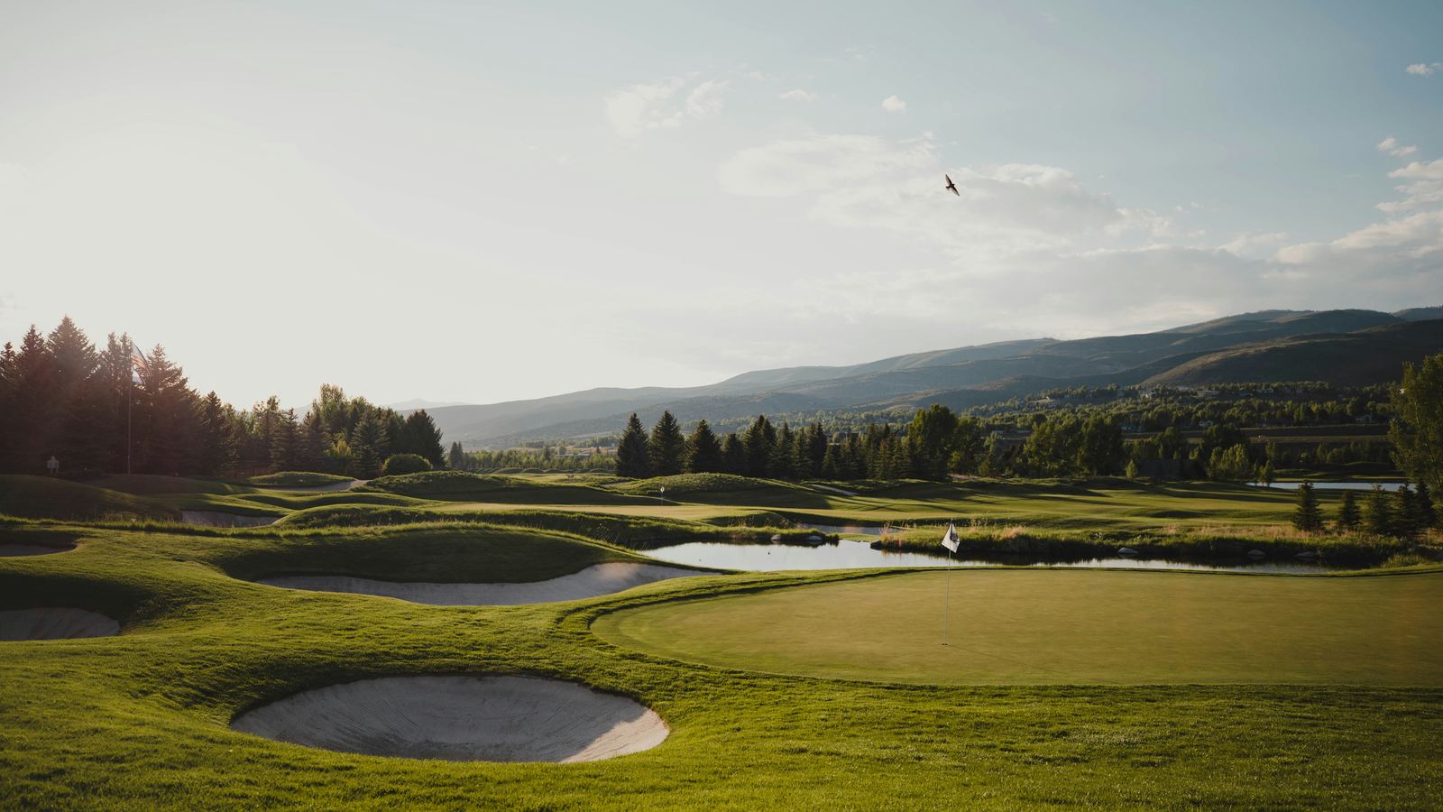 A fairway running through a broad green valley with hills folding away behind it.